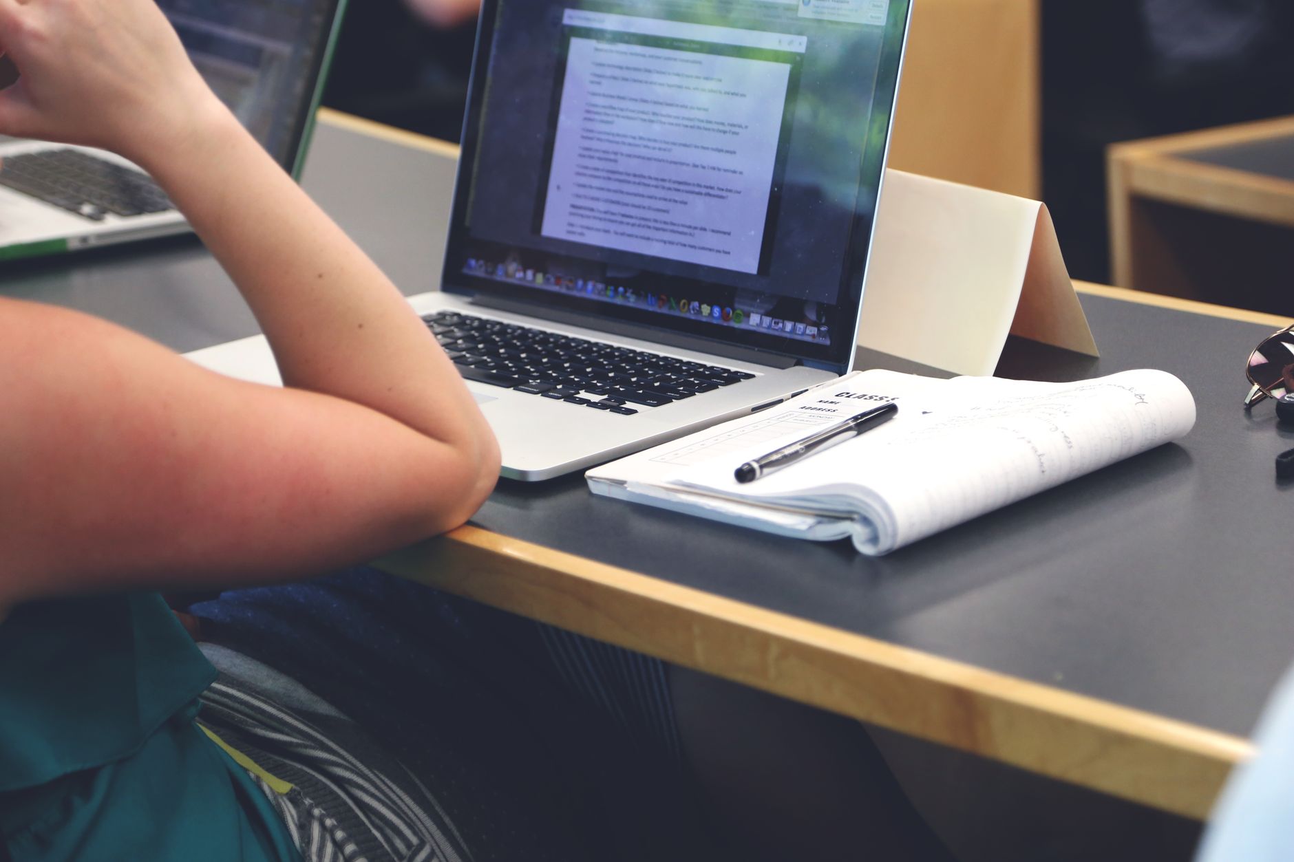 Estudante fazendo anotações em um caderno ao lado de um notebook